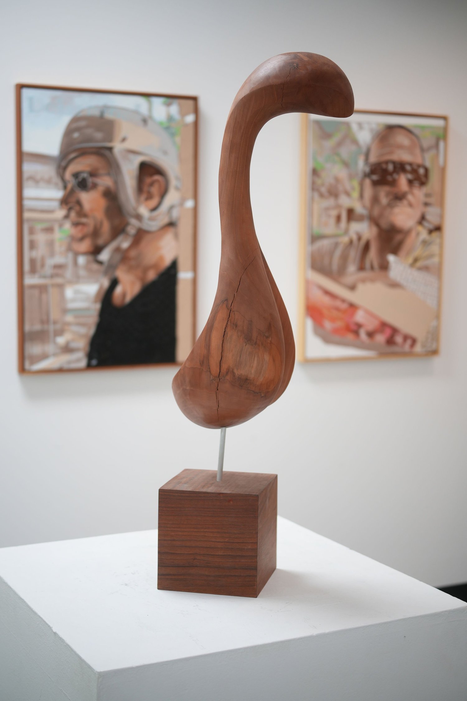 A curved wooden sculpture displayed on a pedestal.