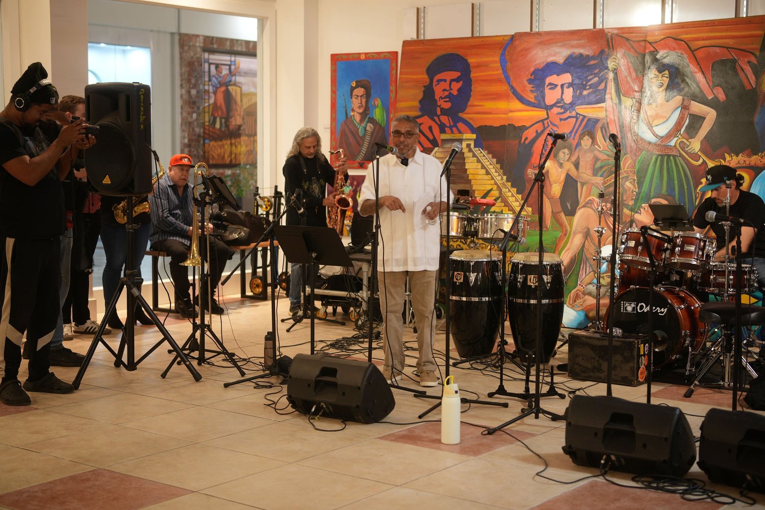 Vocalists and instrumentalists perform before a colorful gallery mural.