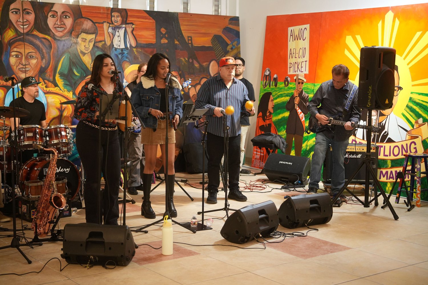 Vocalists and instrumentalists perform before a colorful gallery mural.