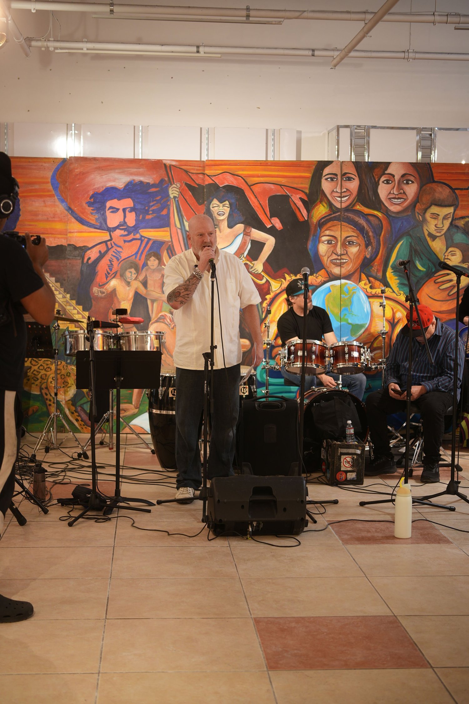 Vocalists and instrumentalists perform before a colorful gallery mural.