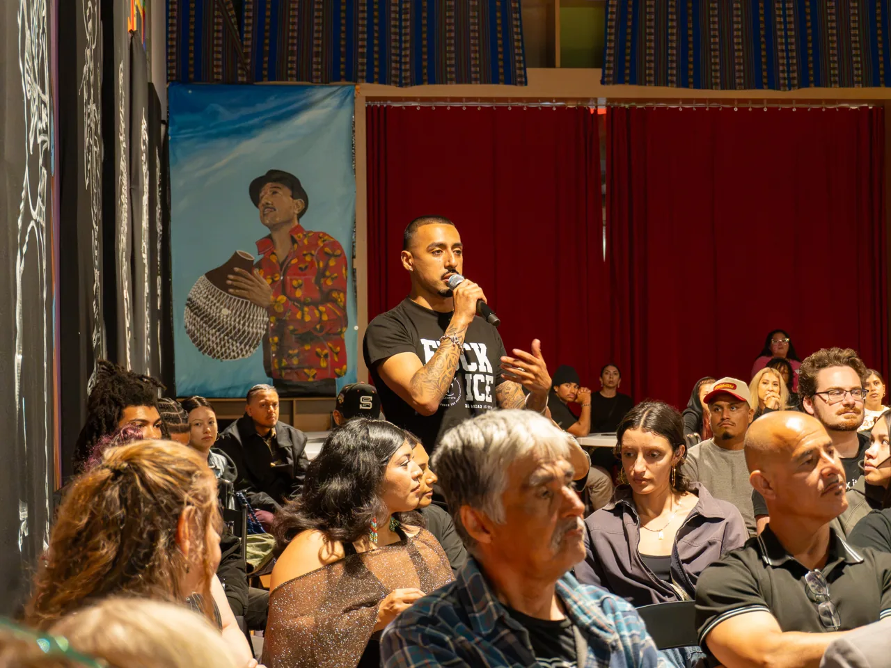 An audience member stands among the seated guests and speaks into a microphone.