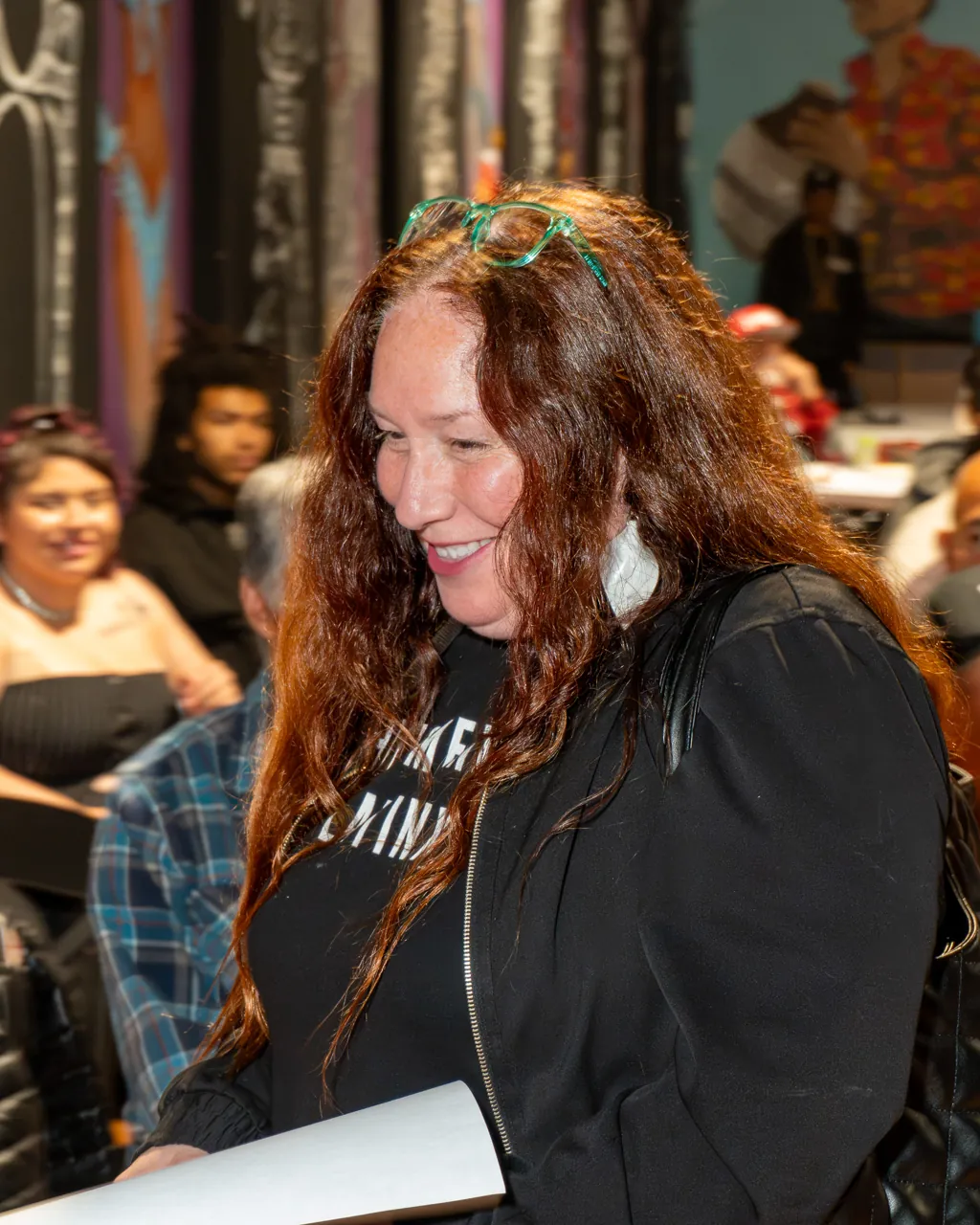 A guest with long curly hair looks down while standing among the seated audience.