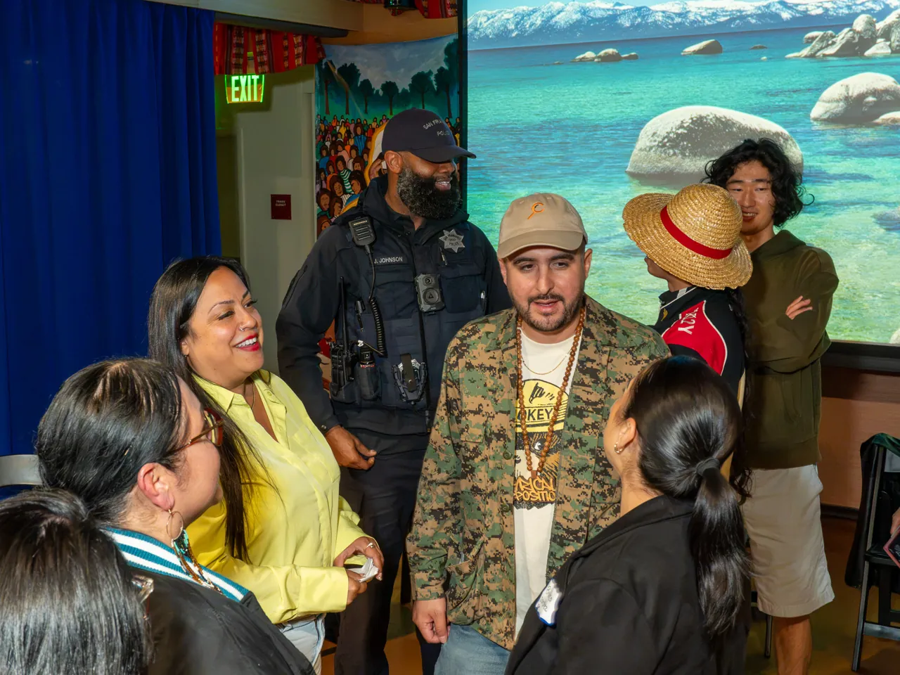 Guests gather closely around a person in a patterned jacket and cap to talk.