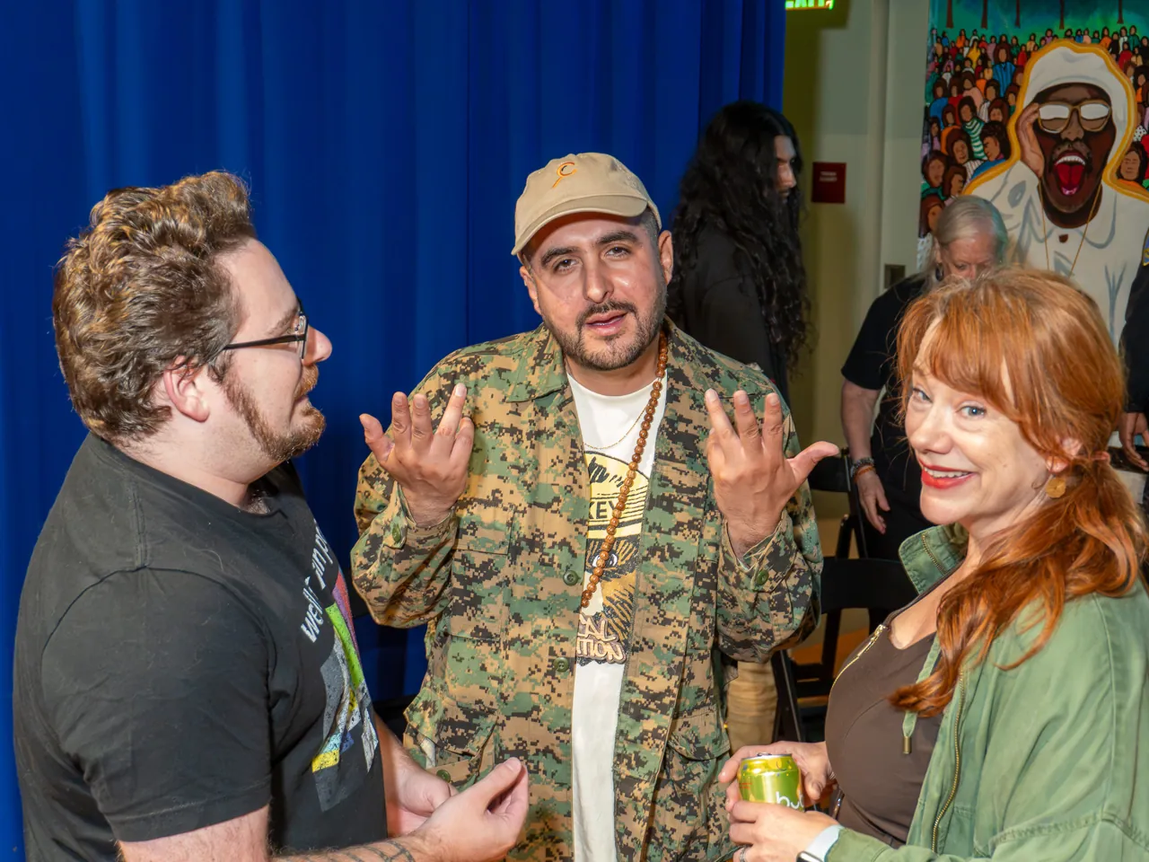 Three guests converse beside the blue curtain, gesturing with their hands.