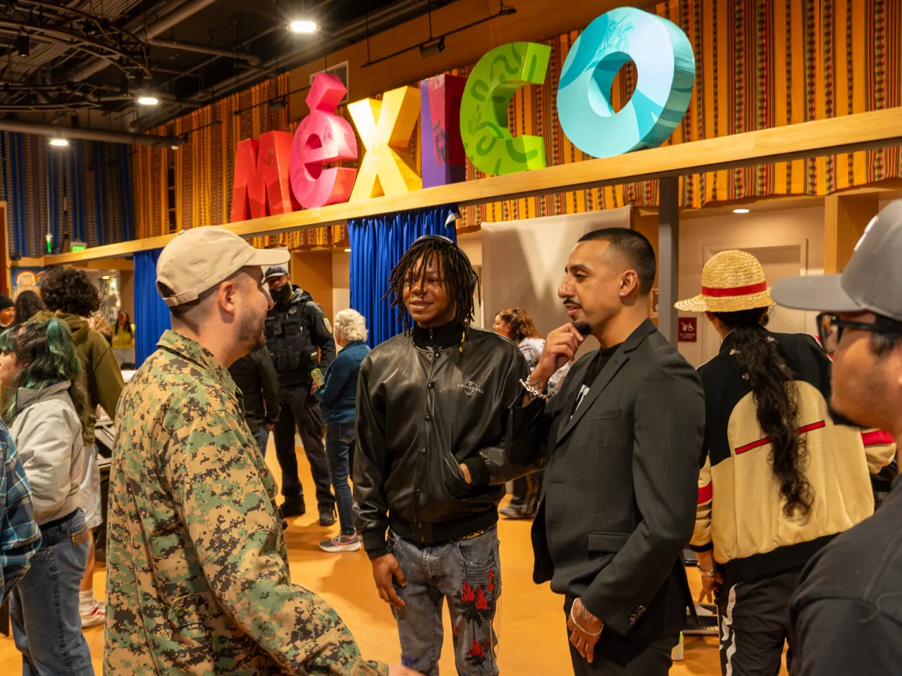 A group talks beneath the colorful MEXICO letters above the blue curtain.