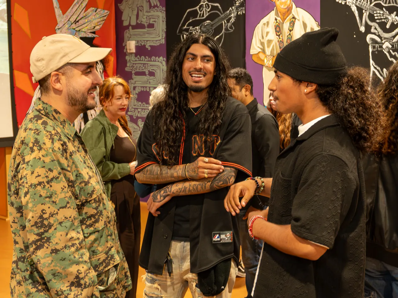 Three guests converse, including a long-haired person and a person in a patterned jacket.