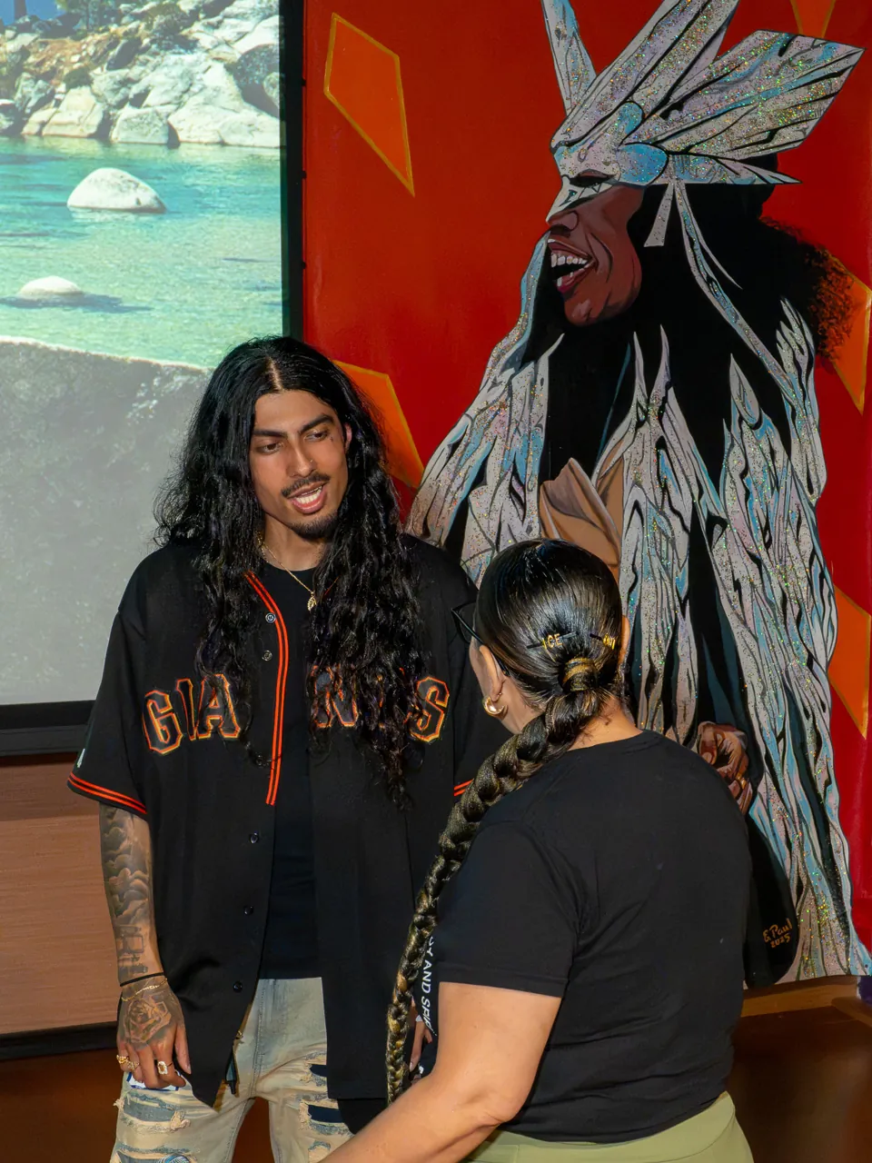 Two guests stand together beside a tall, colorful mural.