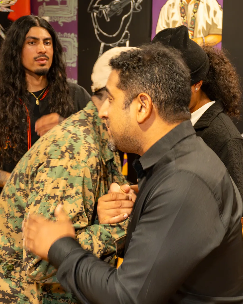 Two guests greet each other with a close embrace as another guest looks on.