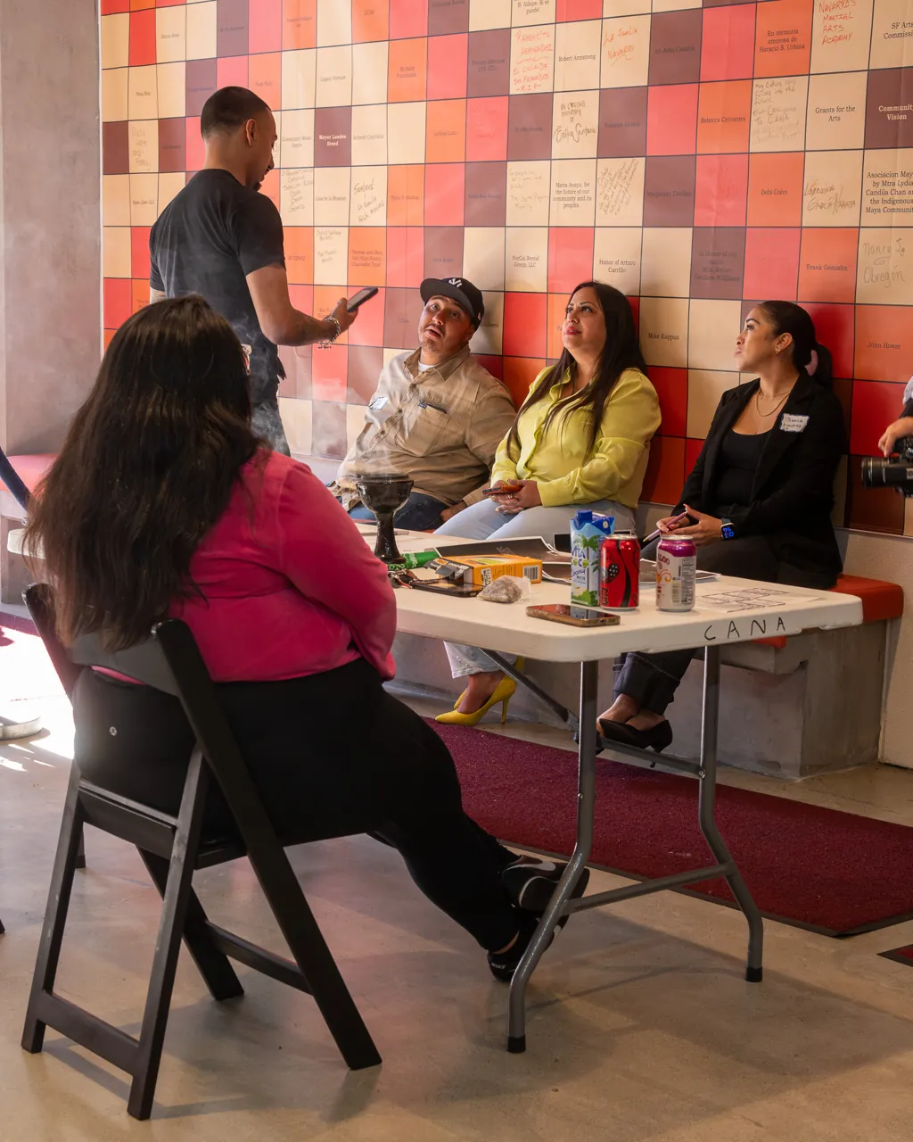 Guests sit and talk around a welcome table against the tiled wall.