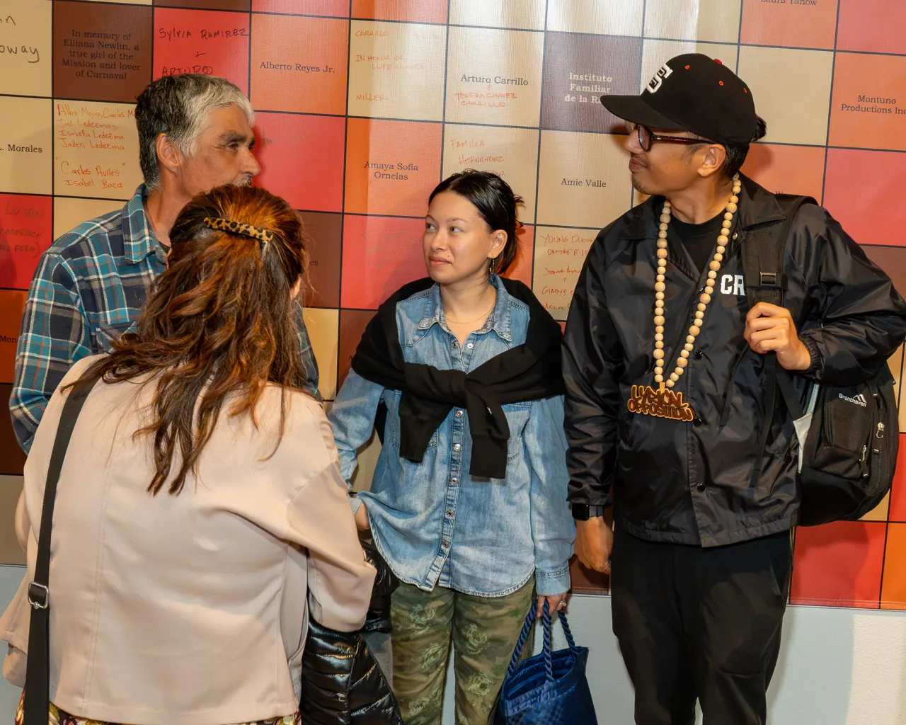 Guests talk together in front of a wall of colored square tiles.