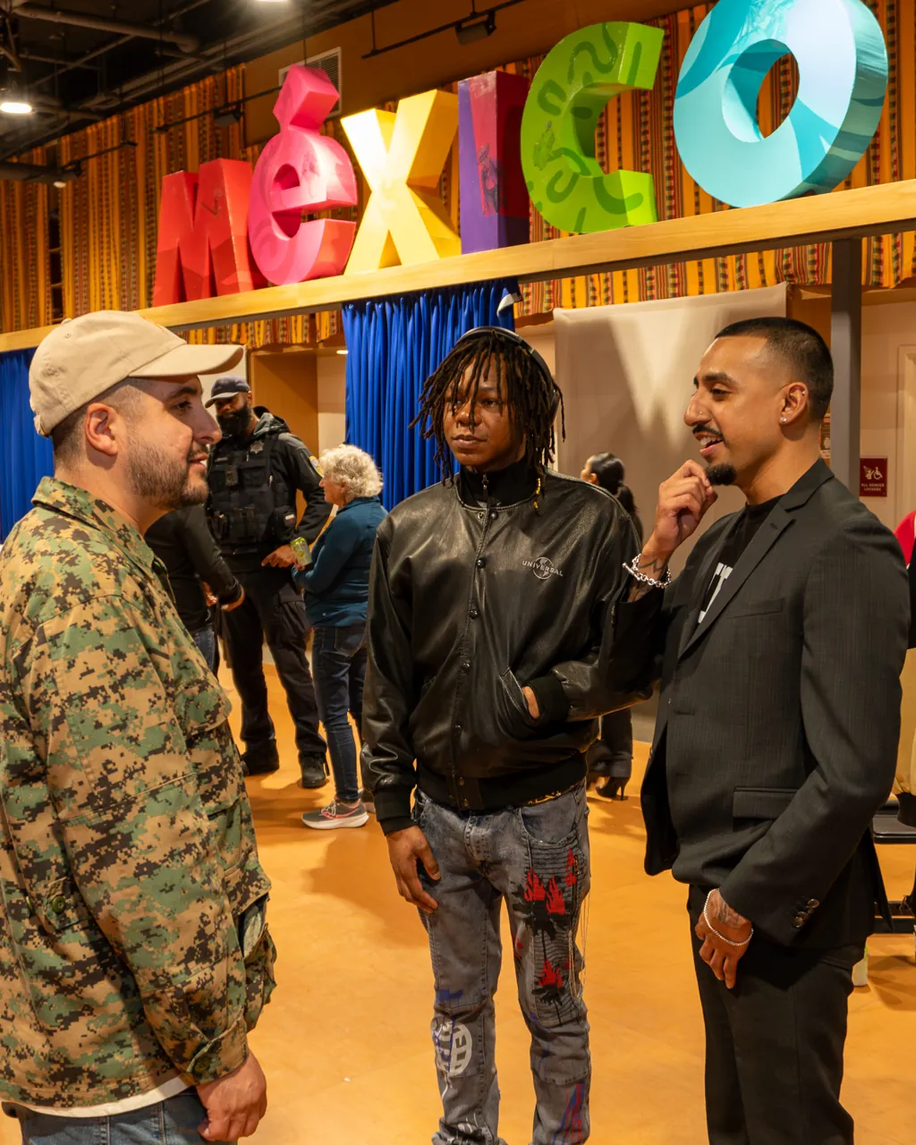 A group talks beneath the colorful MEXICO letters above the blue curtain.