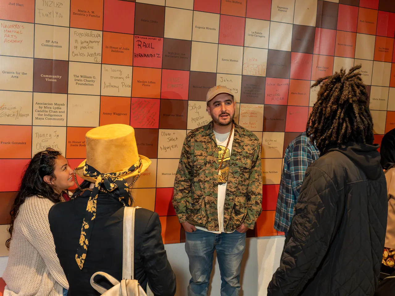 Guests gather near a floor lamp and a wall covered with colored square tiles.