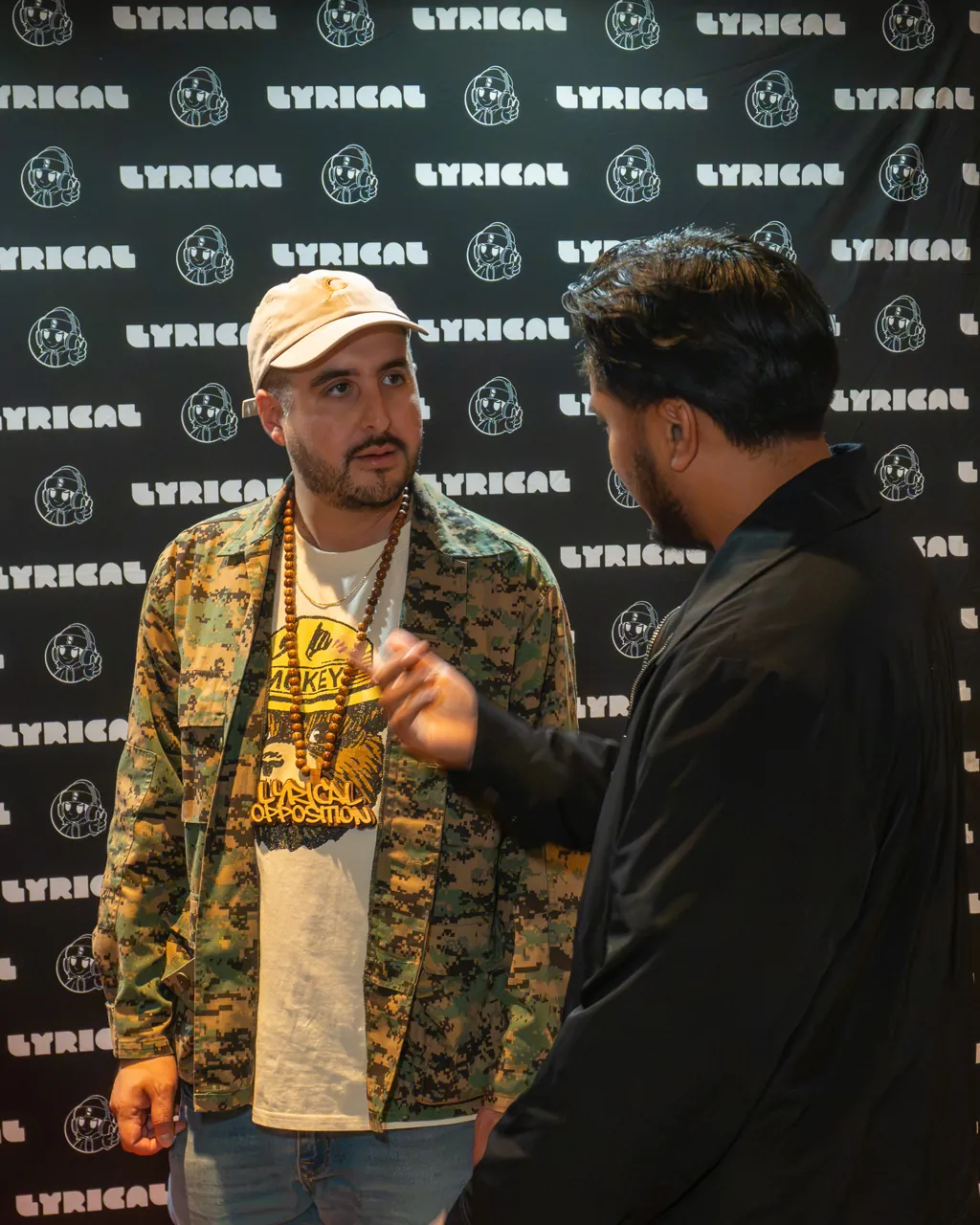 Two guests talk near the photo backdrop, one holding a drink.