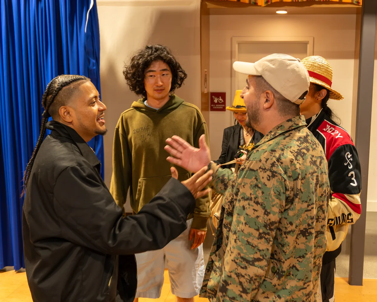 Guests exchange greetings and gestures in a small group near the curtain.