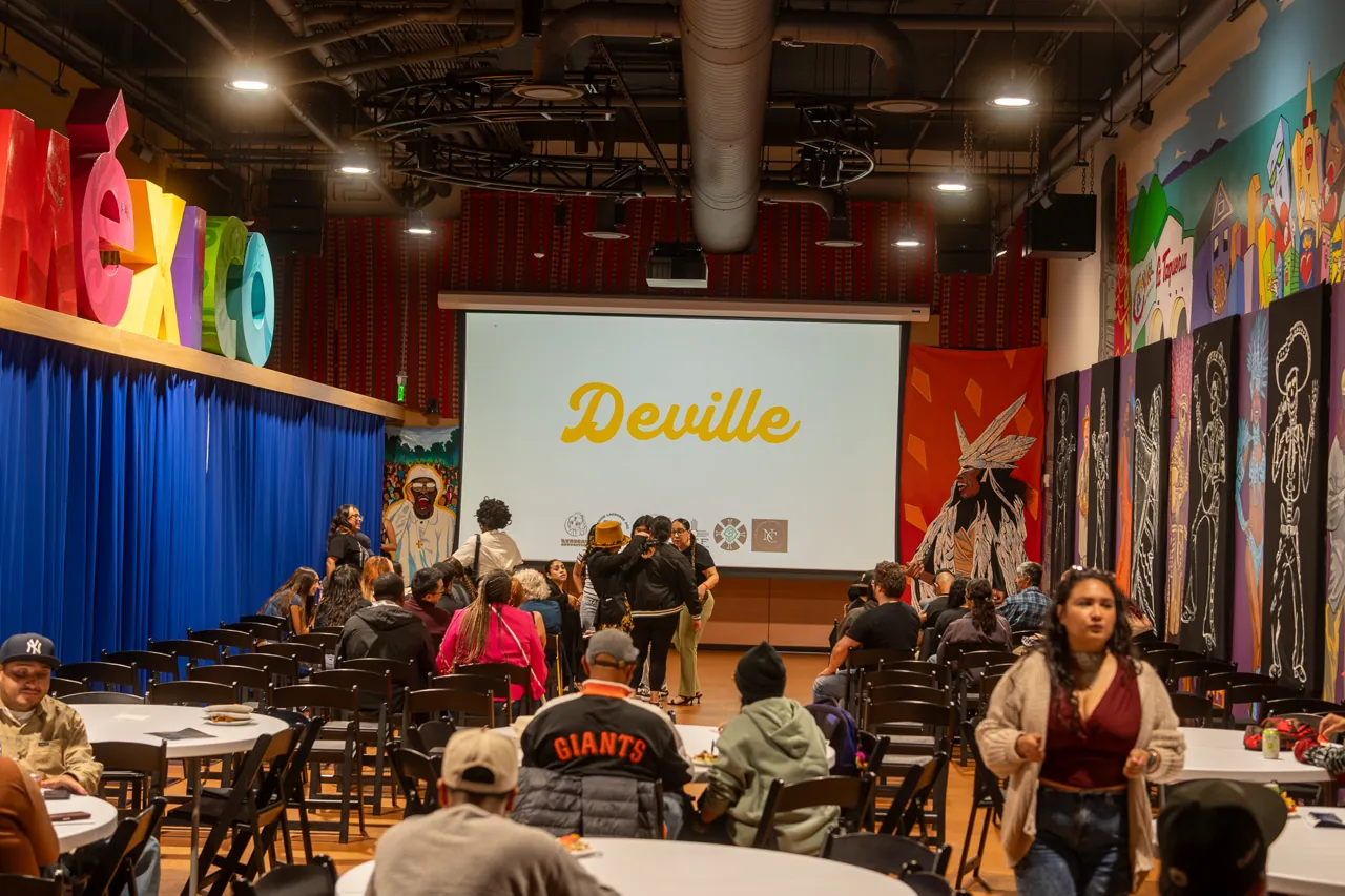 A view down the central aisle toward the projected Deville title and seated guests.