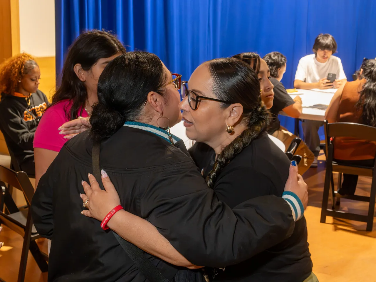 Two guests embrace beside rows of chairs.