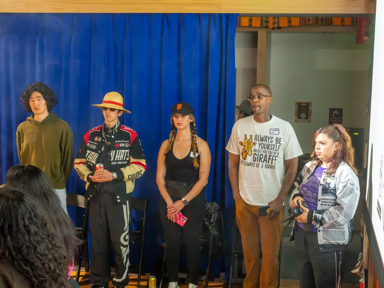 A line of guests stands against the blue curtain at the front of the room.