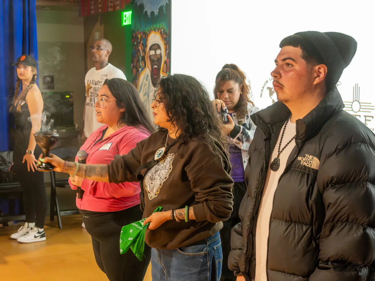 Several people stand together at the front of the room, including a person in pink and a person holding green fabric.