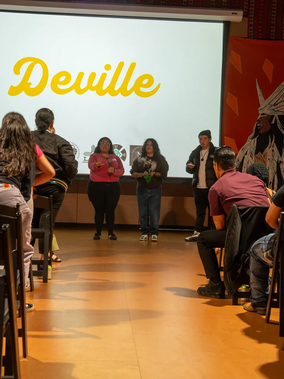 A view down the central aisle toward the projected Deville title and seated guests.
