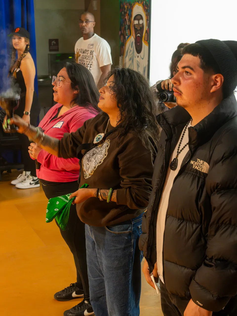 Several people stand together at the front of the room, including a person in pink and a person holding green fabric.