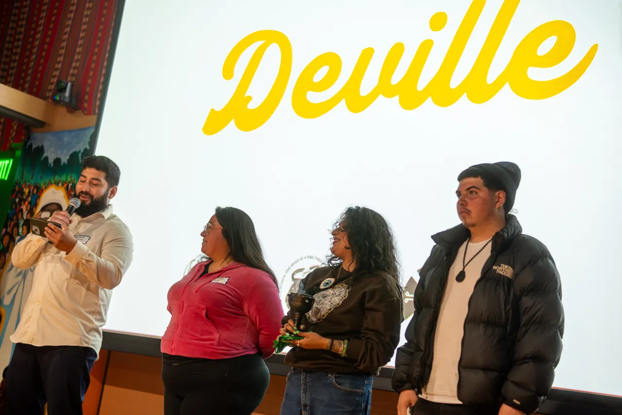 People stand beneath the Deville projection while a person in a light shirt speaks into a microphone.