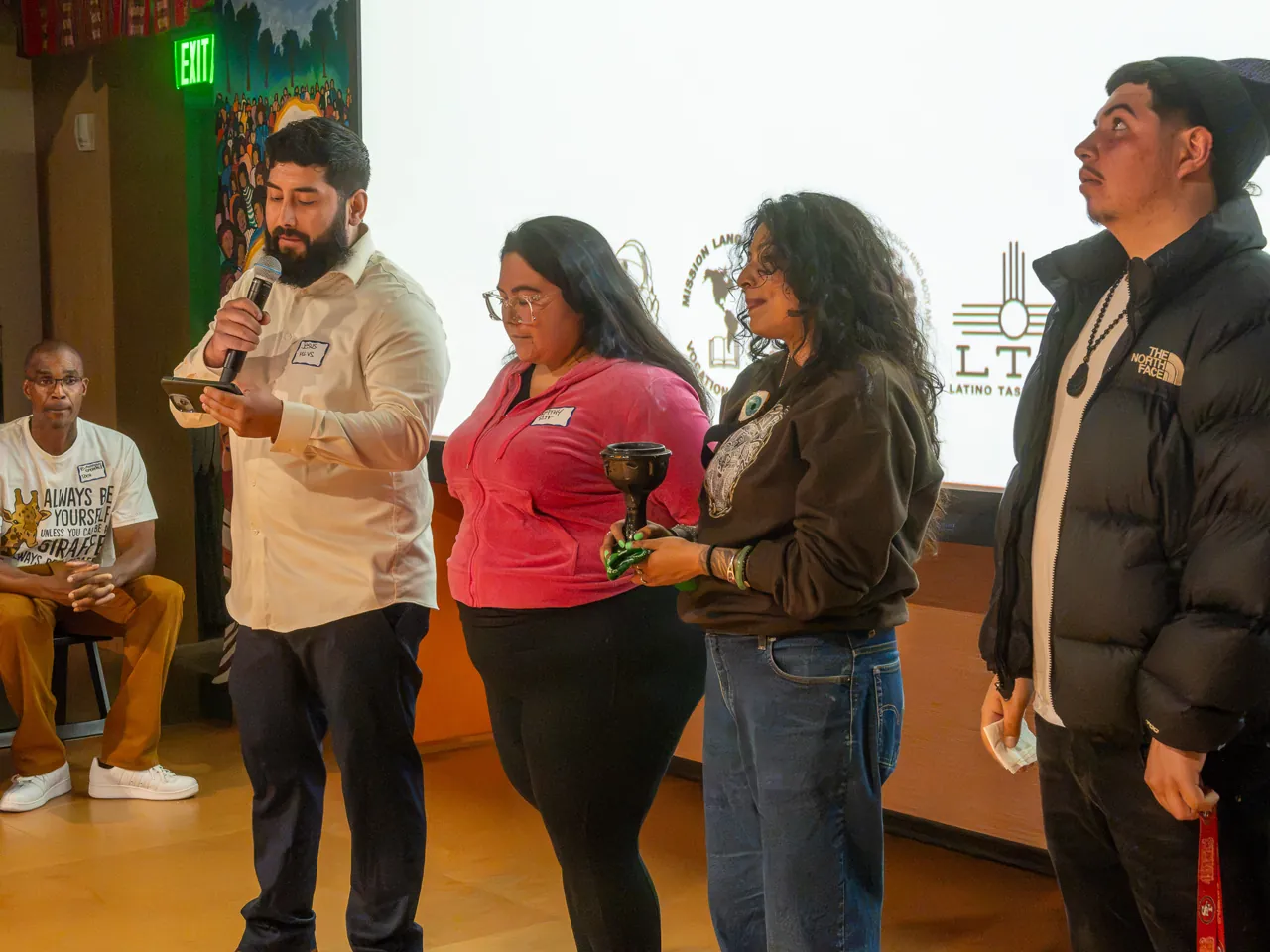 People stand beneath the Deville projection while a person in a light shirt speaks into a microphone.
