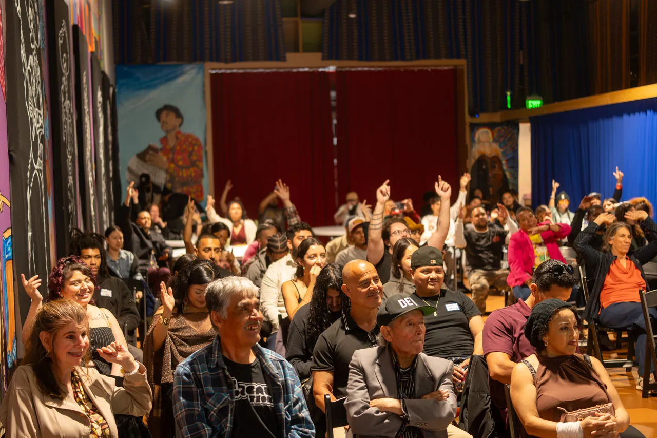 Rows of seated guests watch the program in the mural-lined screening room.