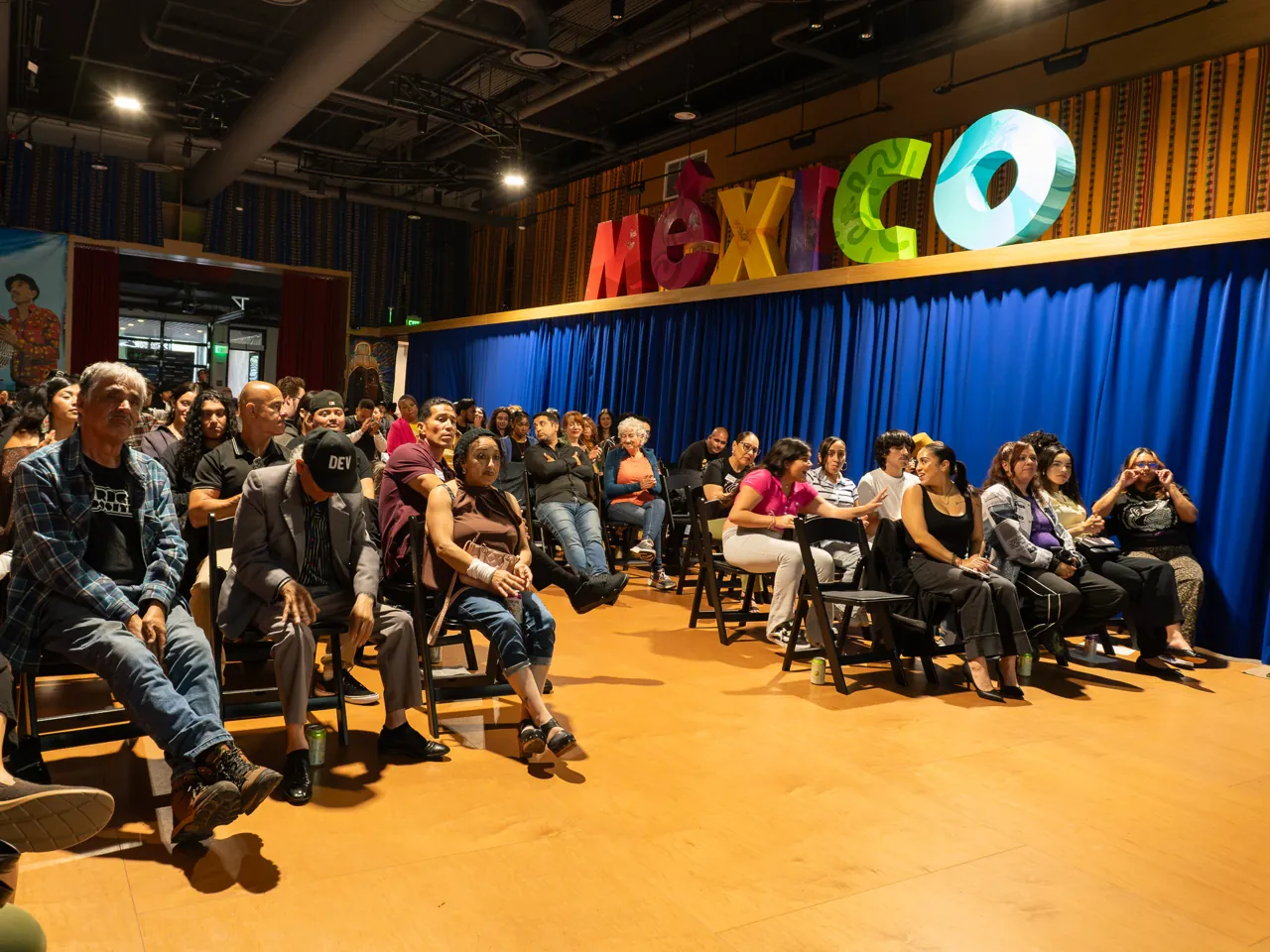 A wide view shows the seated audience beneath large colorful MEXICO letters.