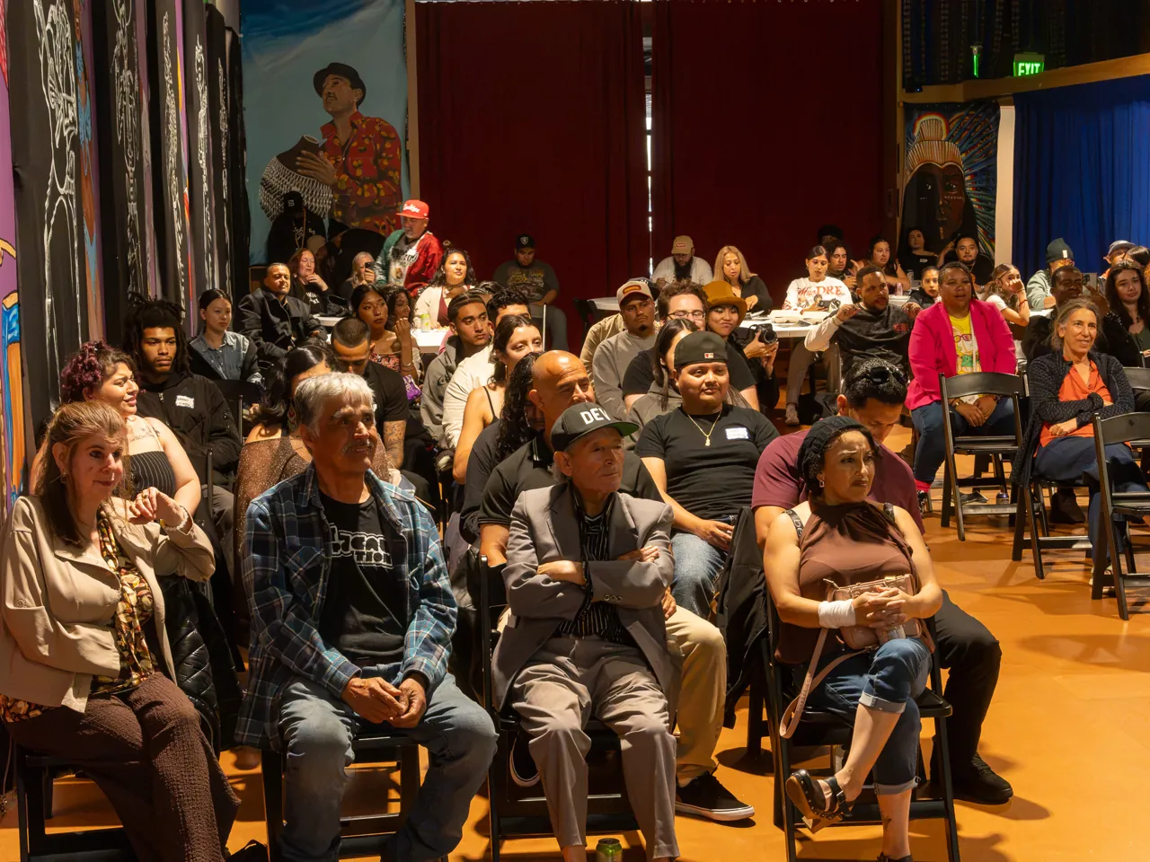 Rows of seated guests watch the program in the mural-lined screening room.