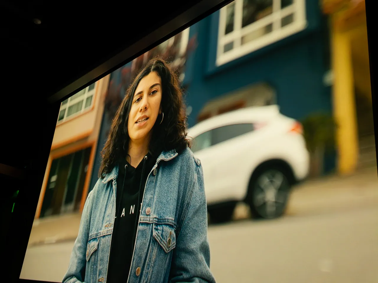 The projection screen shows a person in a denim jacket standing outdoors.