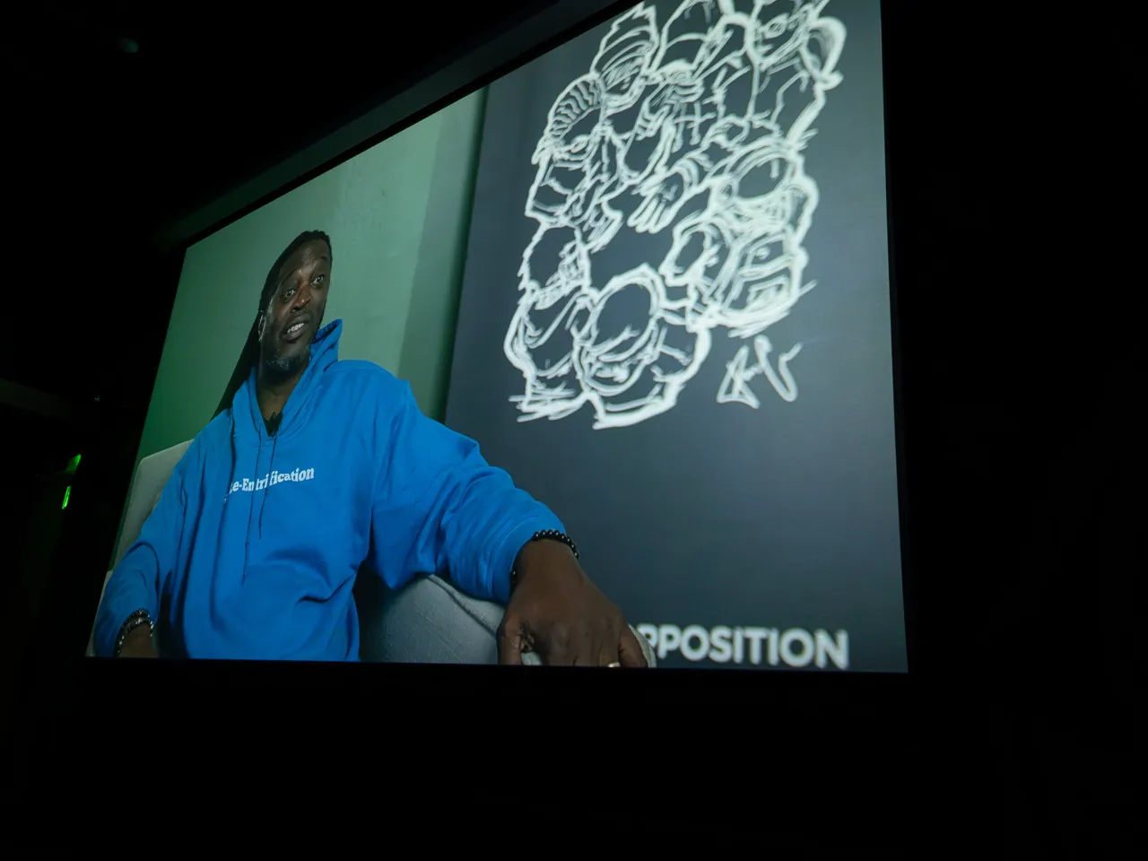 A projected video shows a seated person in a blue shirt beside a white floral graphic.