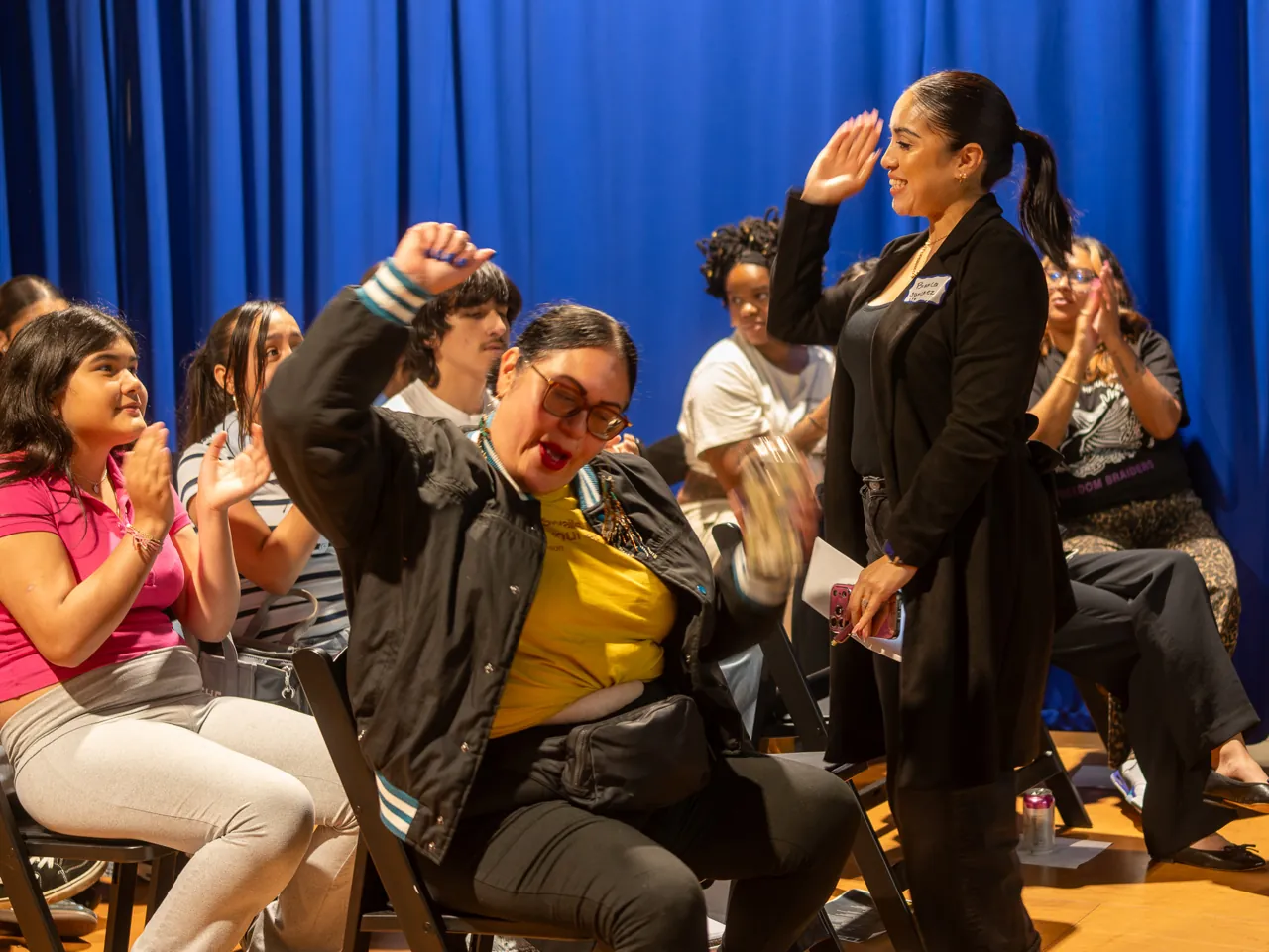 Two audience members stand and raise their hands among the seated guests.