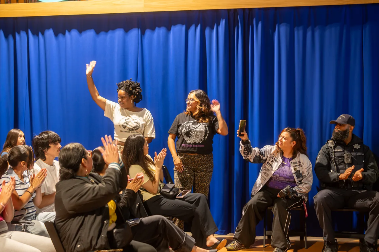 Guests raise their hands while seated beside the blue curtain.