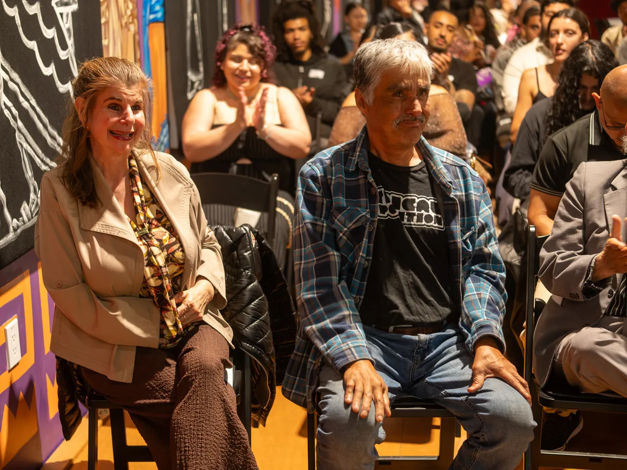 Two guests sit beside each other in the audience, smiling toward the front of the room.
