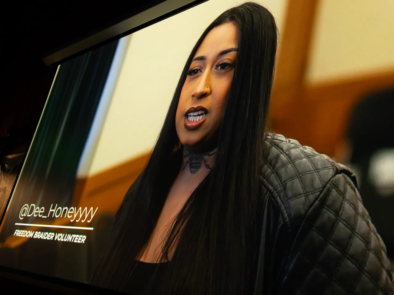 A projected interview shows a long-haired person in a plaid jacket.