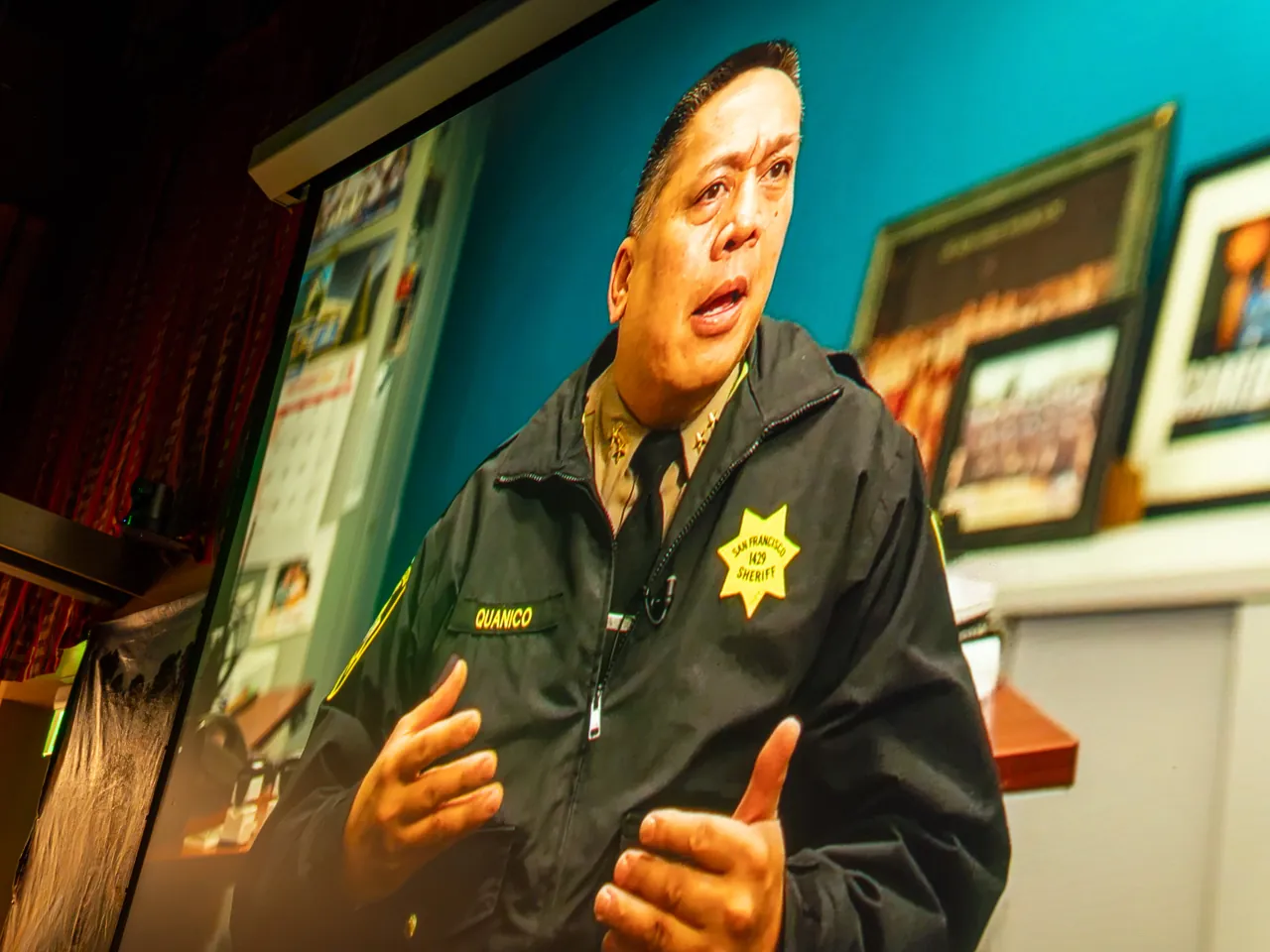 A projected interview shows a uniformed officer gesturing while speaking.