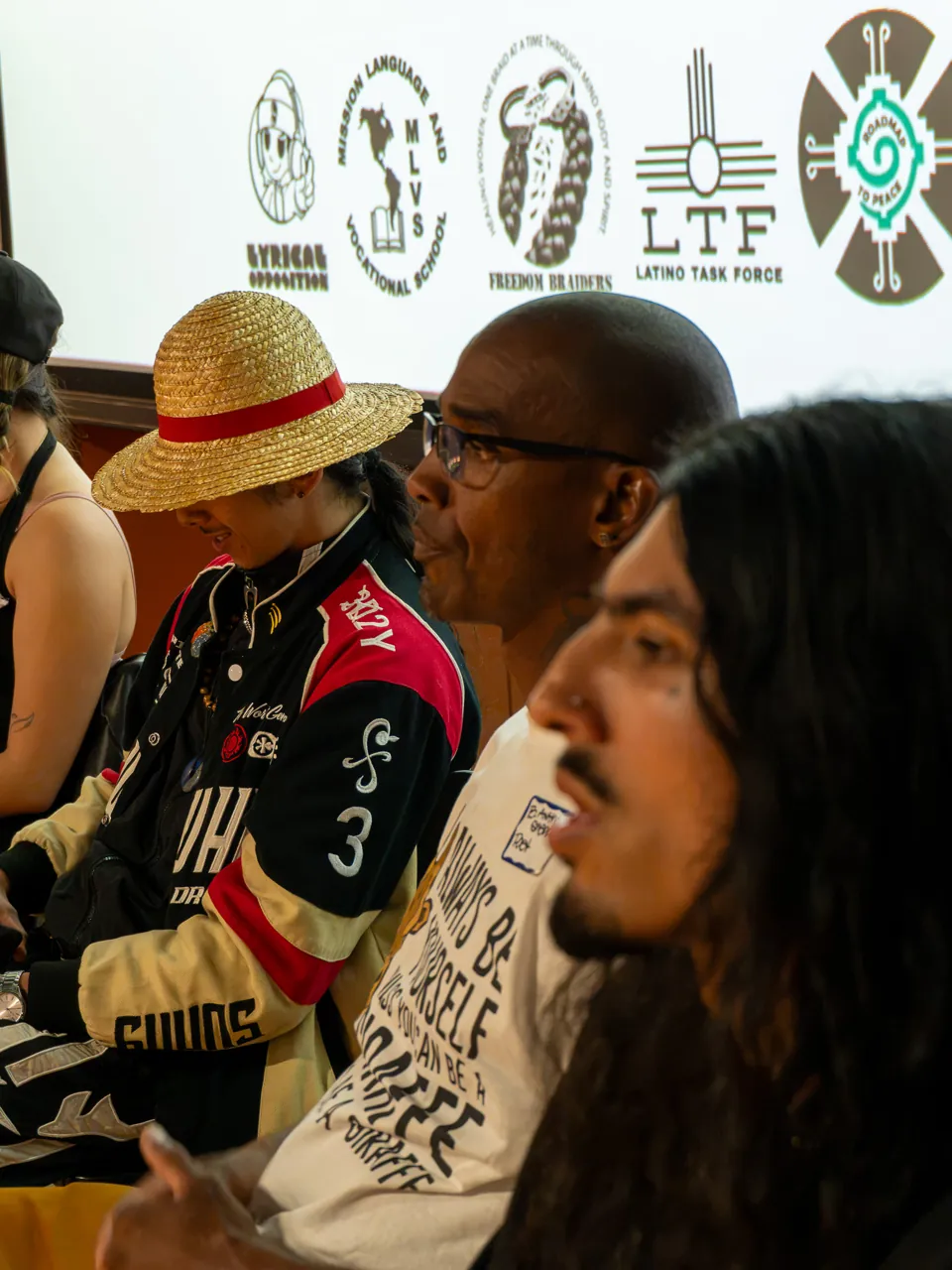 A close view of seated panel participants listening beside the screen.