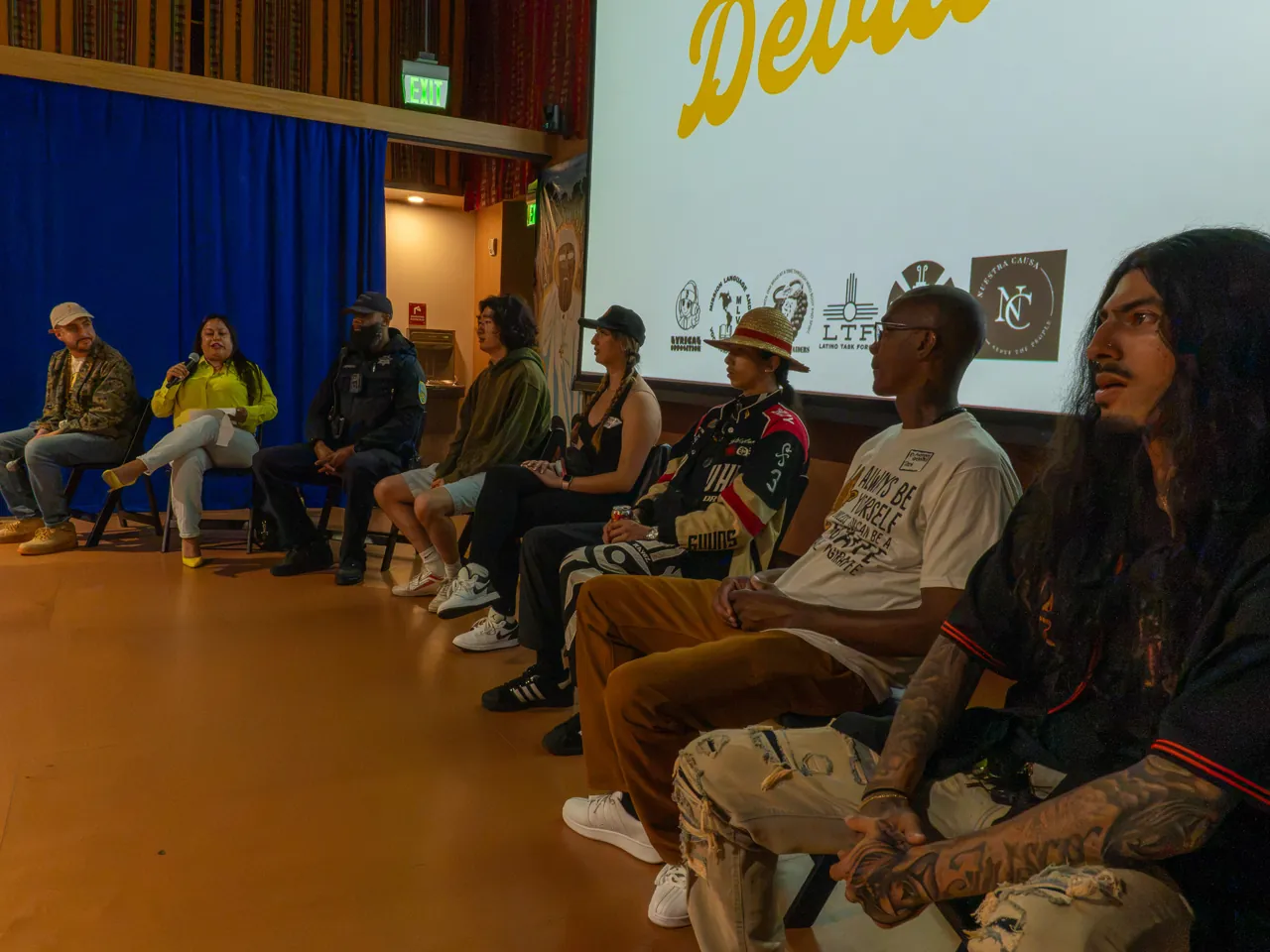 Panel participants sit in a row beneath the Deville projection.