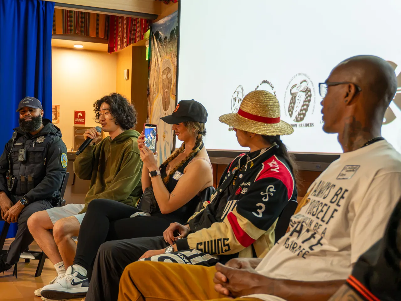 Panel participants sit in a row beneath the Deville projection.