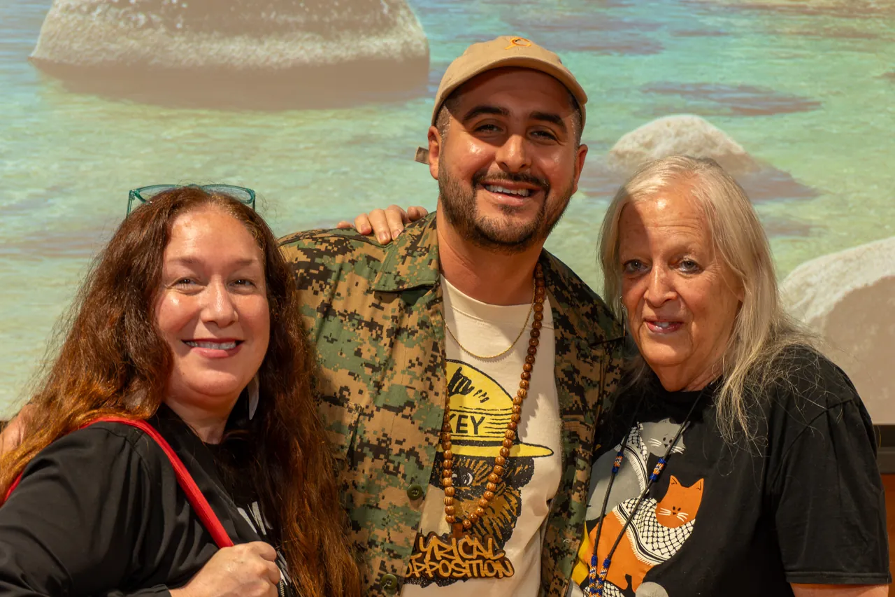 Three guests smile for a photograph in front of a landscape mural.