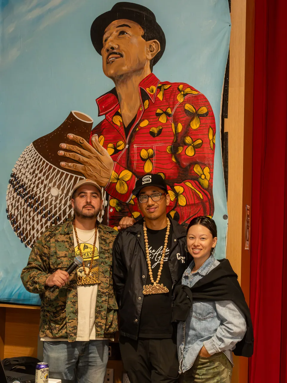 Two guests pose in front of a mural featuring a figure in red.