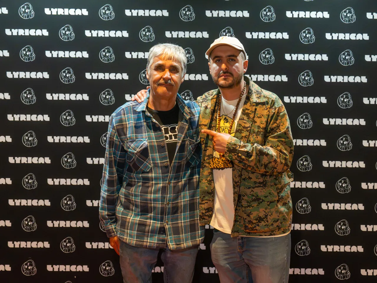 Two guests pose together in front of the black event photo backdrop.