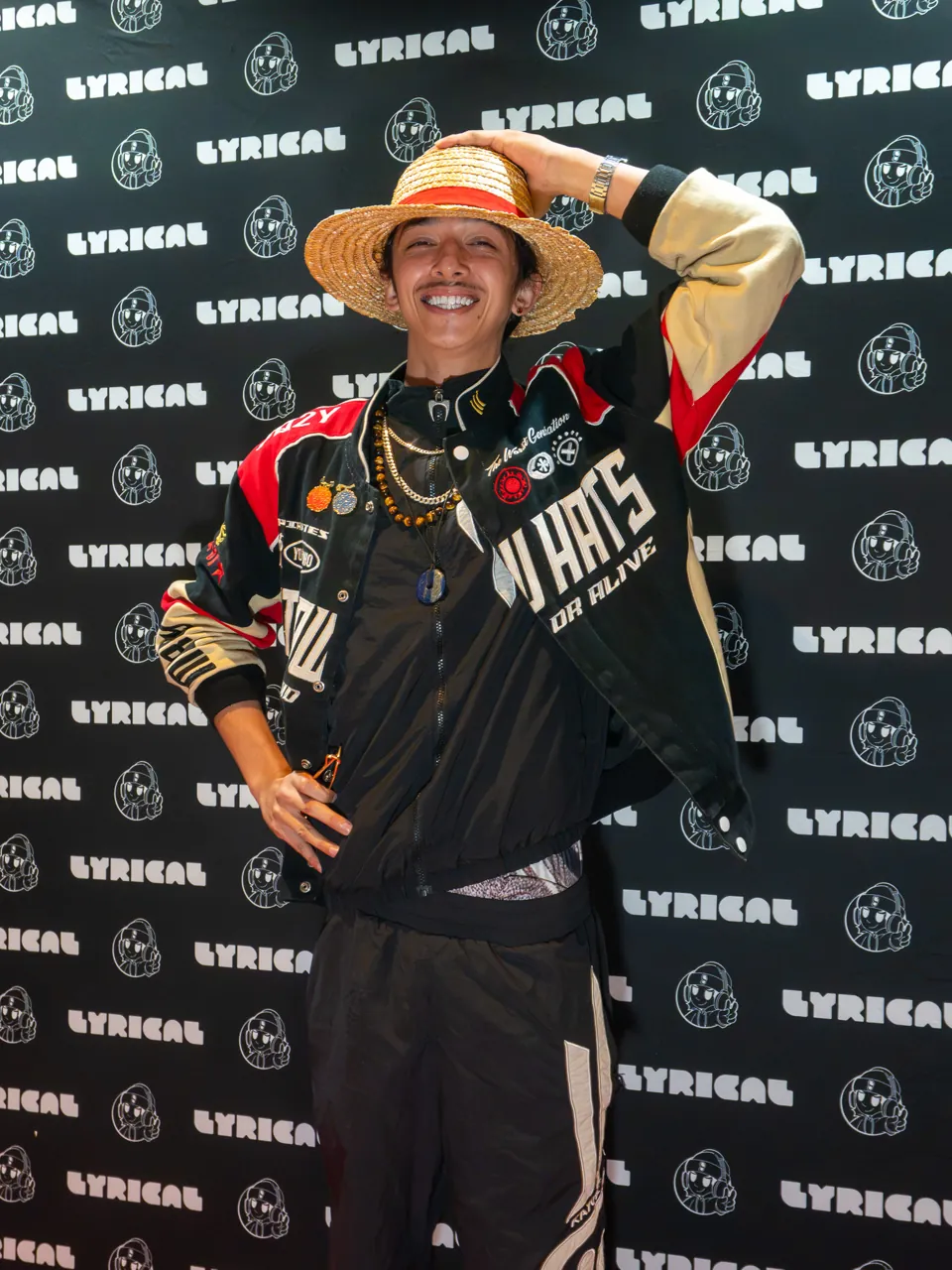 A guest in a straw hat and racing jacket poses with one hand behind their head.