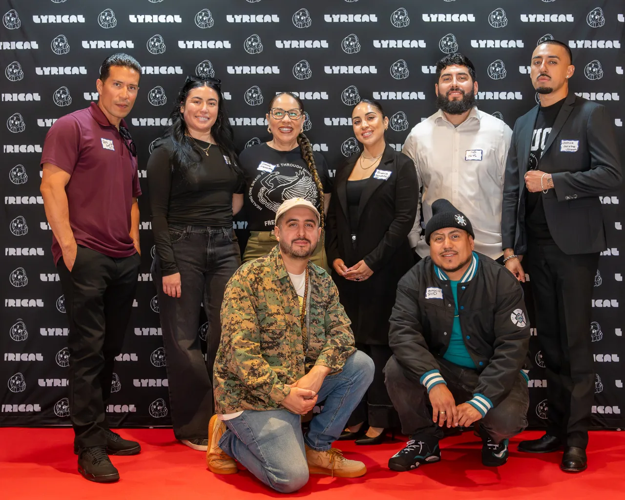 A group poses at the event photo backdrop, with two guests crouching in front.