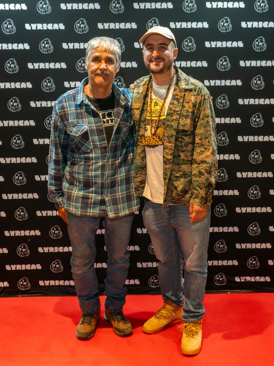 Two guests pose together in front of the black event photo backdrop.