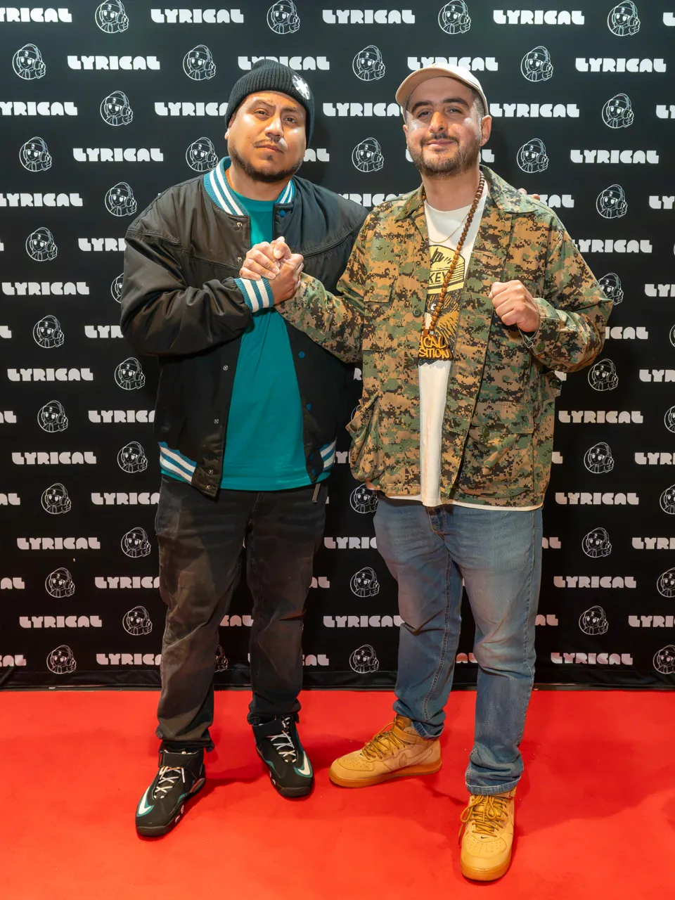 Two guests pose side by side at the black event photo backdrop.