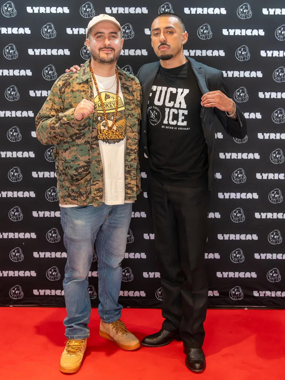 Two guests stand together on the red carpet in front of the event photo backdrop.