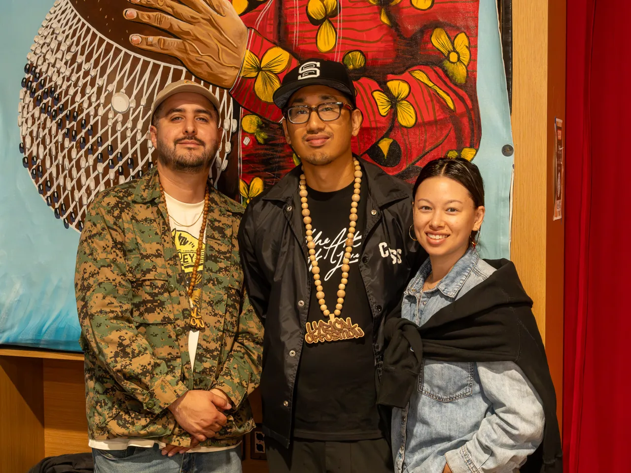 Three guests pose together in front of the colorful mural.