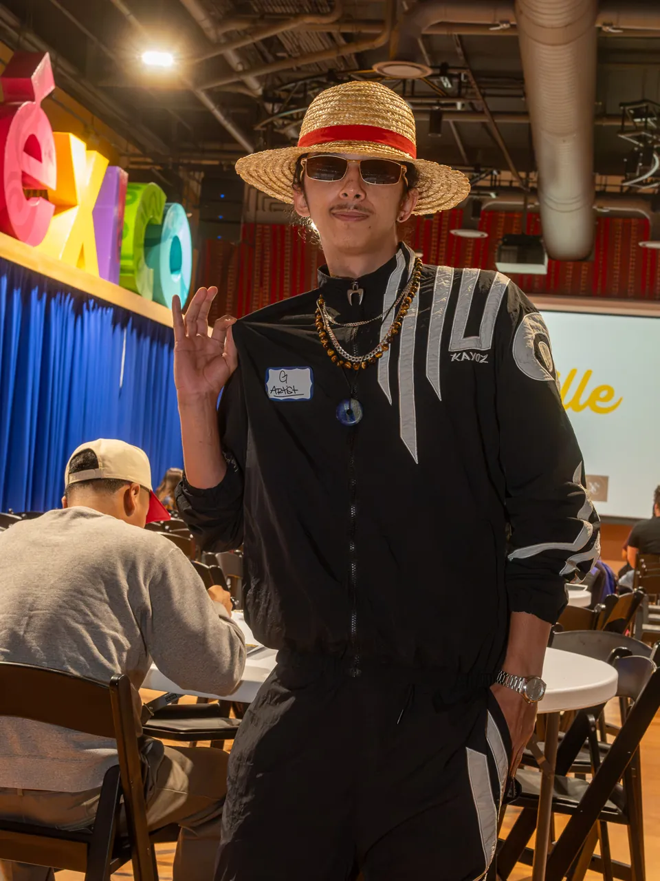 A guest in a straw hat poses in the screening room with one arm raised behind their head.