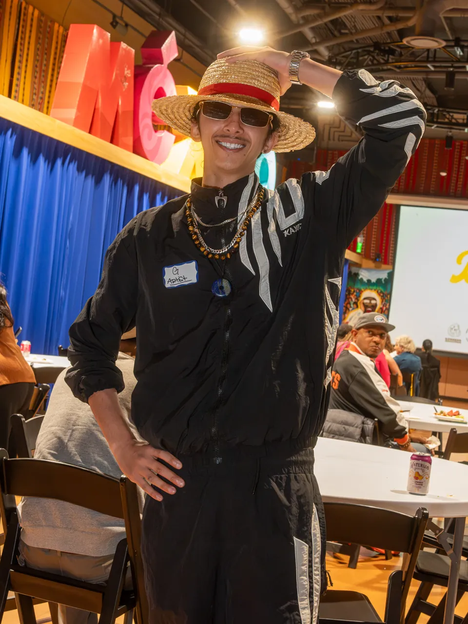 A guest in a straw hat poses in the screening room with one arm raised behind their head.